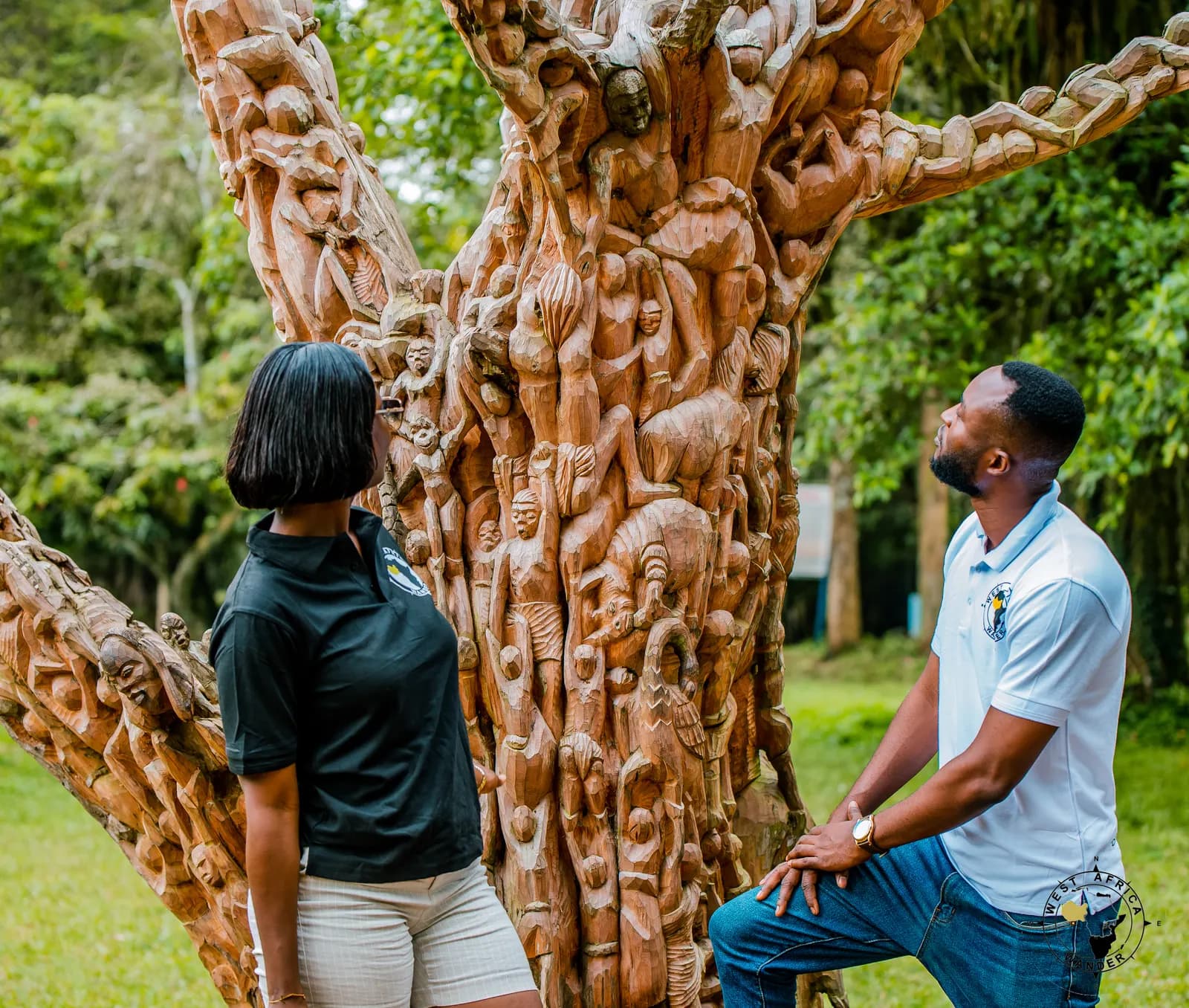 Two travellers looking up at a tree trunk carved all over with figures
