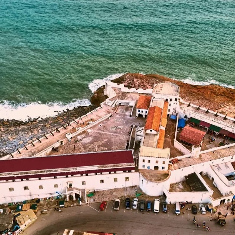 An aerial view of Cape Coast Castle on the rocky shore, with the sea behind it
