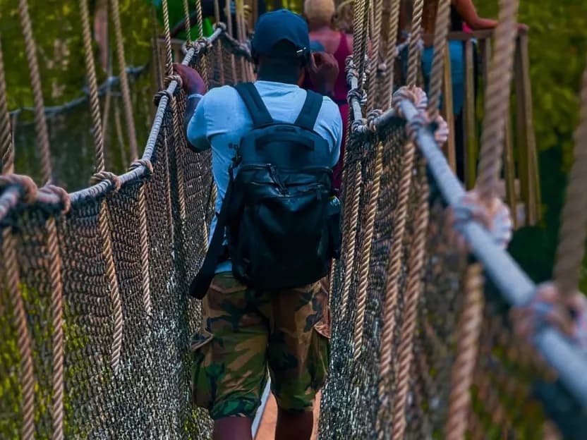 A visitor with a backpack walks along the rope canopy walkway at Kakum National Park