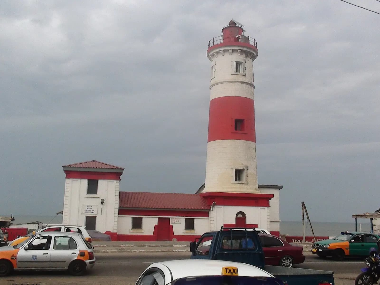 The red and white Jamestown lighthouse in Accra, with taxis on the road in front