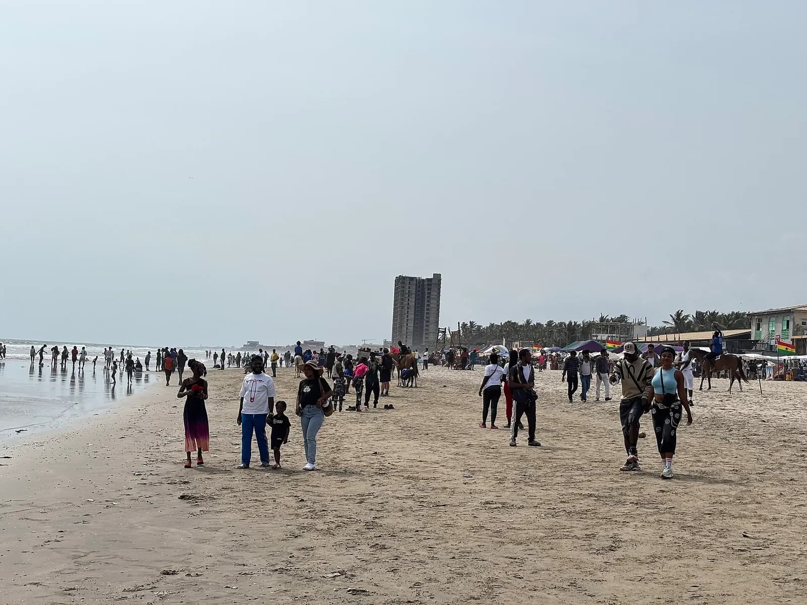 Visitors walking along the wide sand of Labadi Beach in Accra, with horses and stalls behind