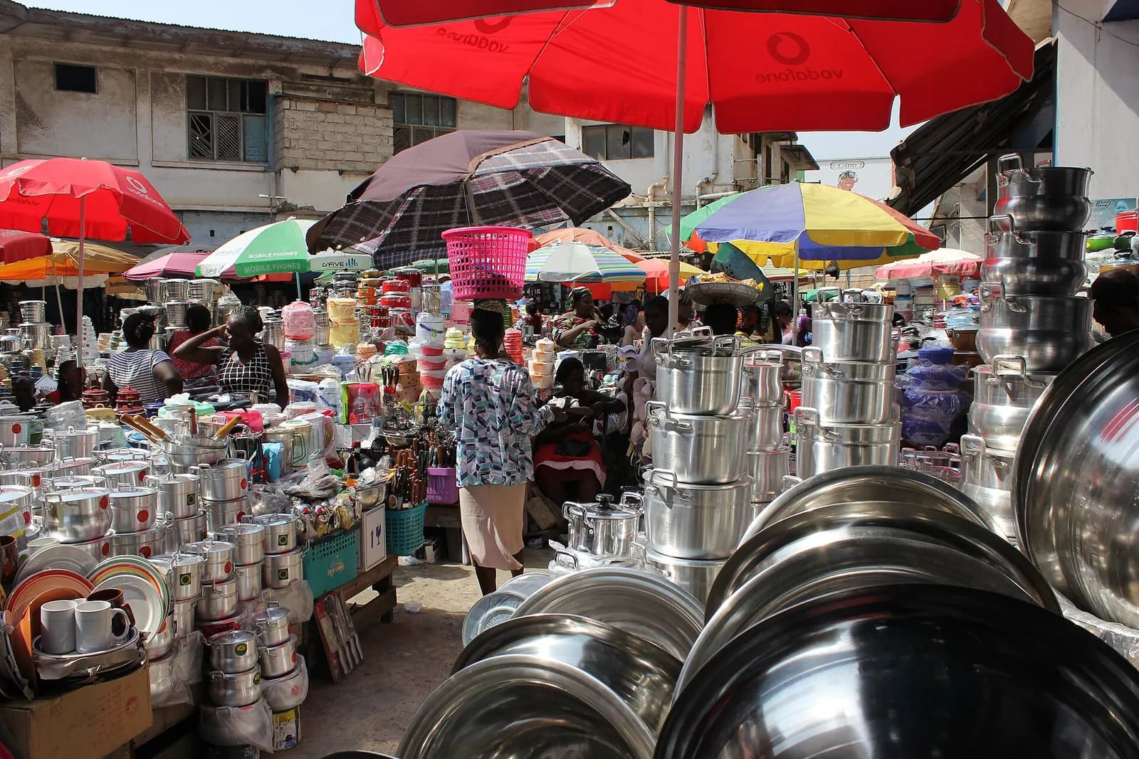 Stalls of steel cooking pots under bright umbrellas at Makola Market in Accra