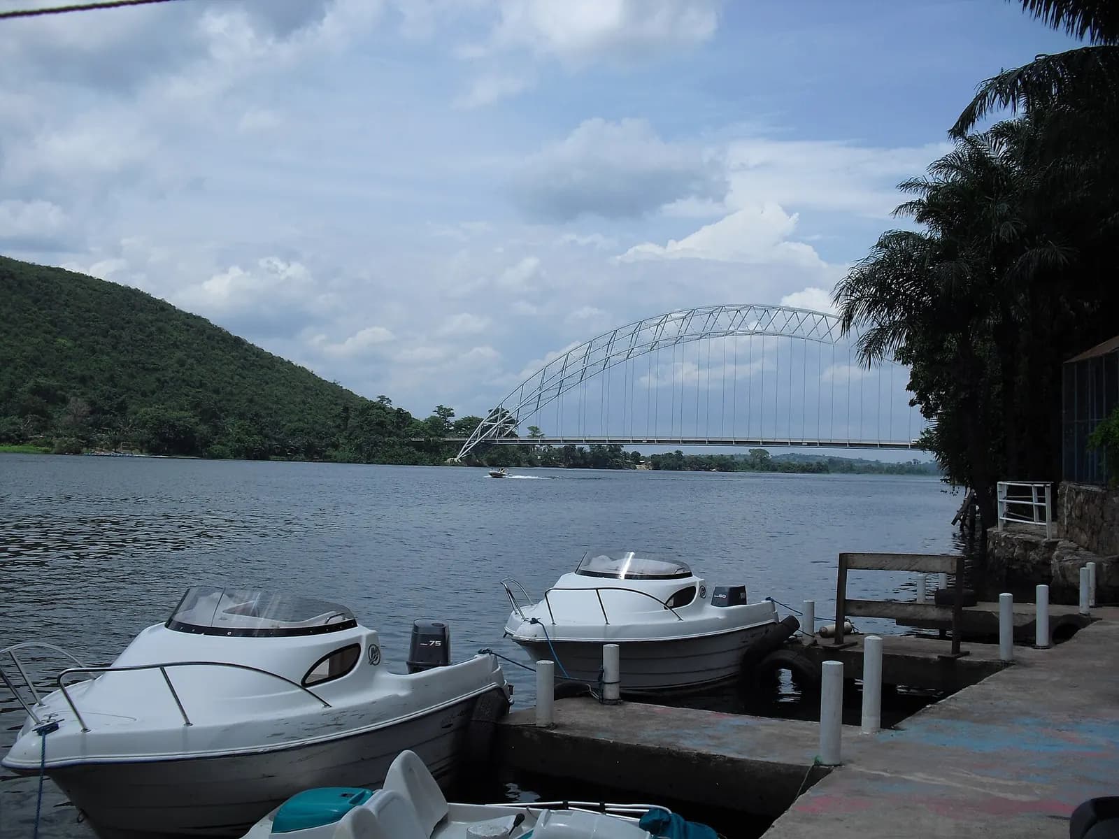 The white steel arch of the Adomi Bridge over the Volta, seen from a jetty with moored speedboats