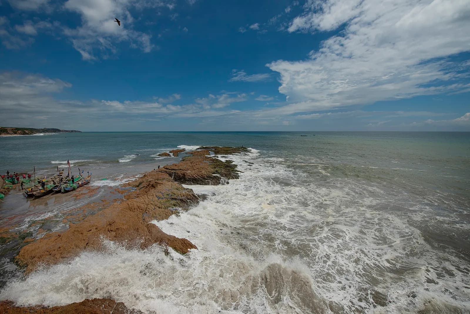 Waves breaking over a rocky point at Cape Coast, with fishing canoes pulled up on the sand
