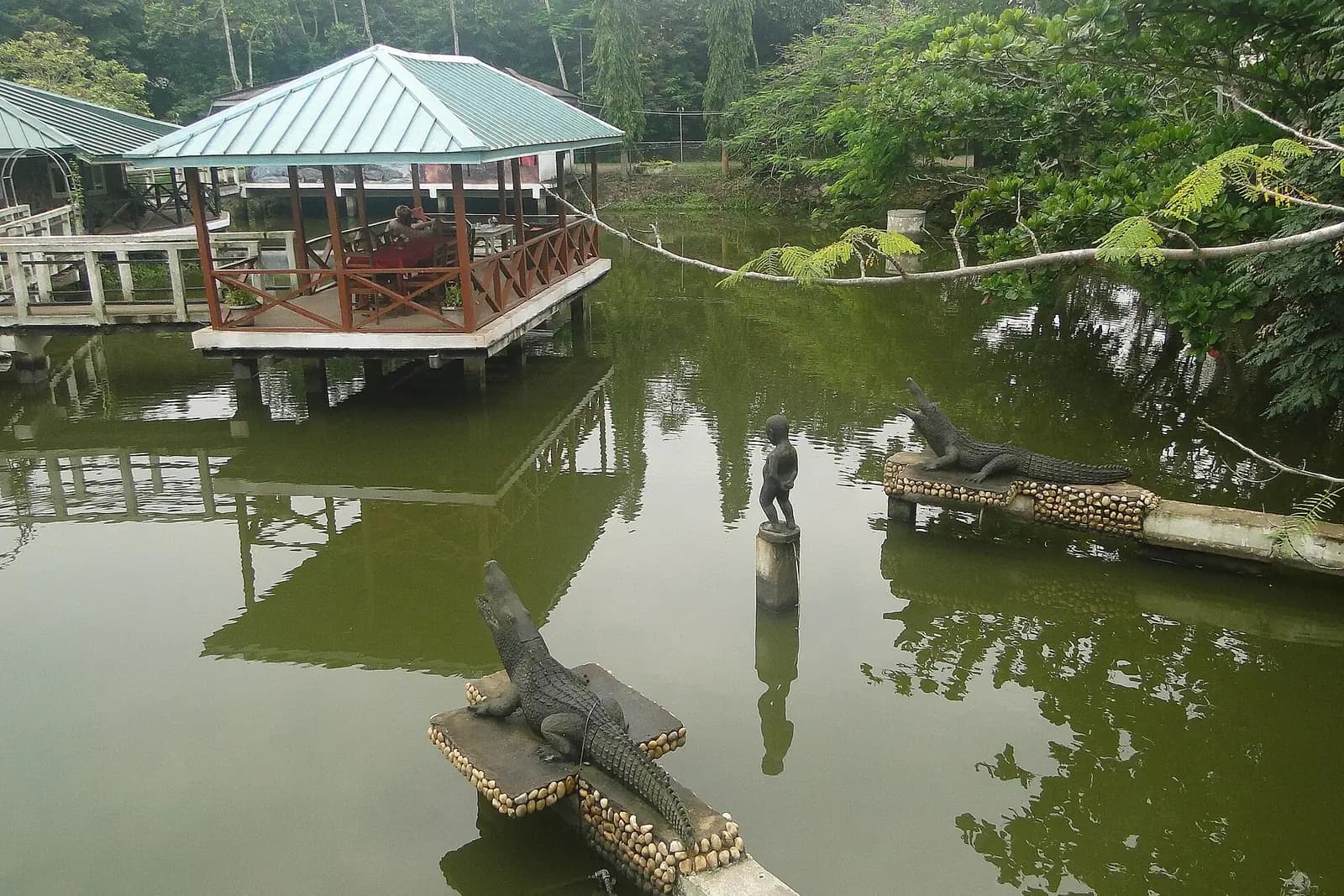 The pond at Hans Cottage Botel, with a raised dining pavilion and crocodile sculptures on stone ledges
