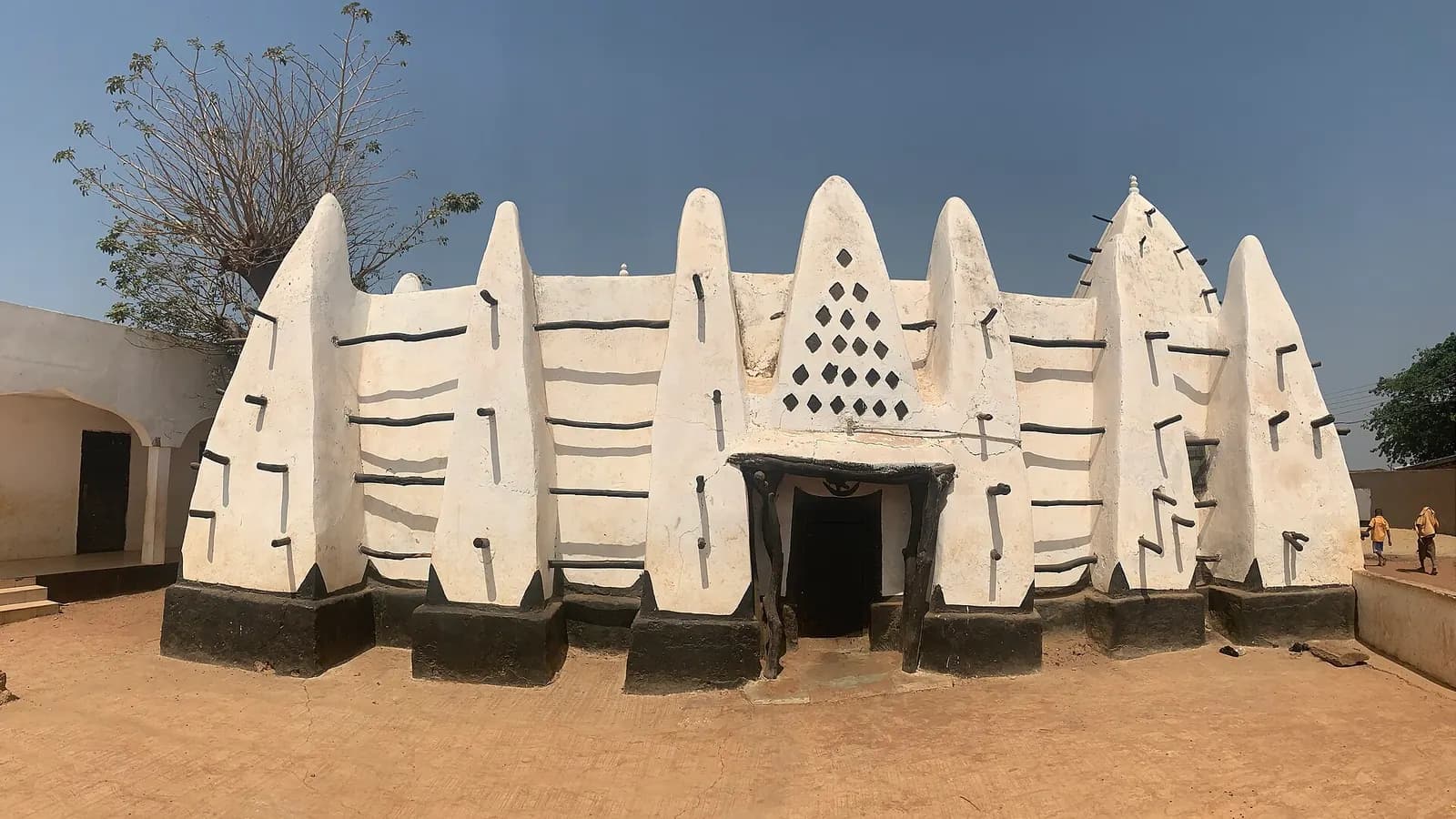 The white mud walls and pointed buttresses of the Larabanga Mosque under a clear blue sky