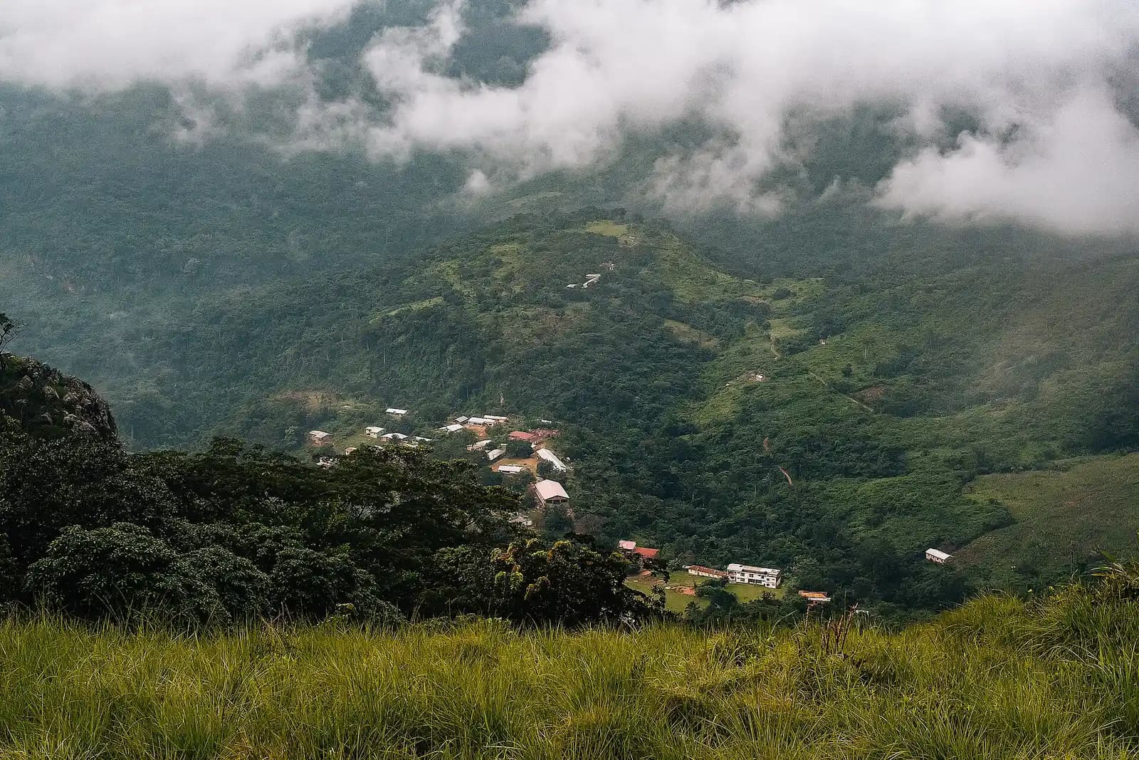 Houses of Amedzofe in a green valley below cloud-covered hills in the Volta Region